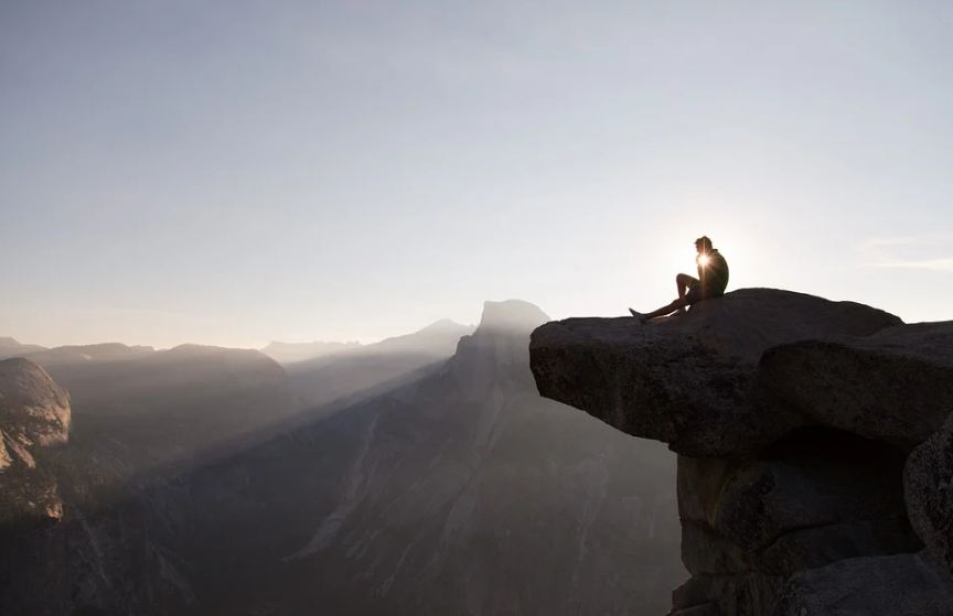 Hiker sitting at the edge of a stone formation at early morning with the sunrise at the Yosemite National Park