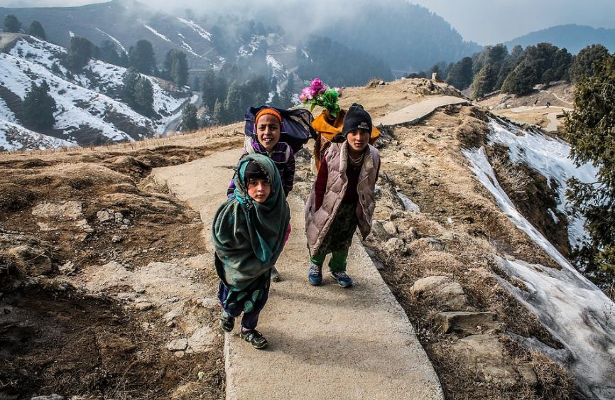 Three children with their backpacks on a trail overlooking mountain ranges