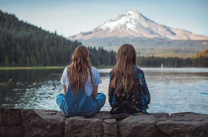 Two women sitting facing the lake with a full view of a standing mountain