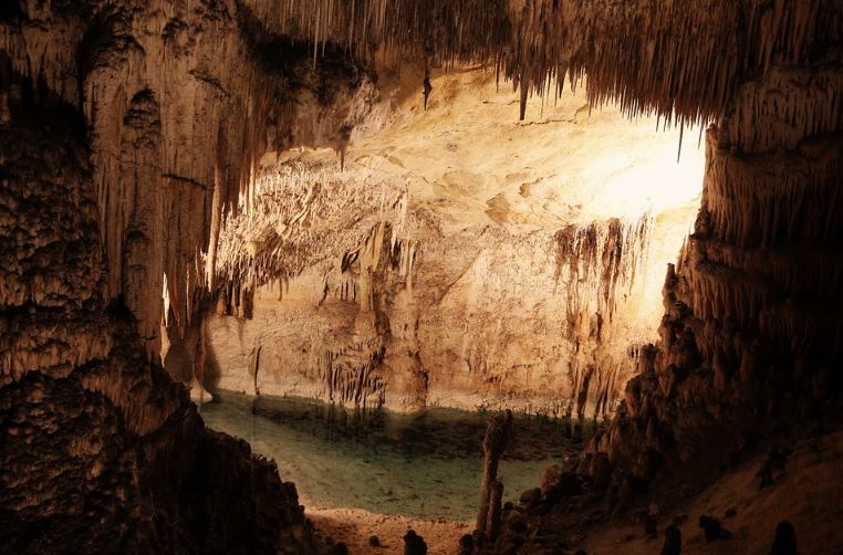 Stalactite and stalagmite inside the cavern with water and a light enters