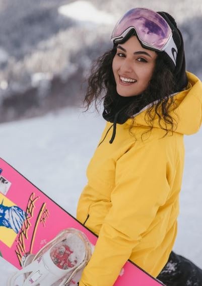 woman in a yellow hoodie holding a pink and white snowboard