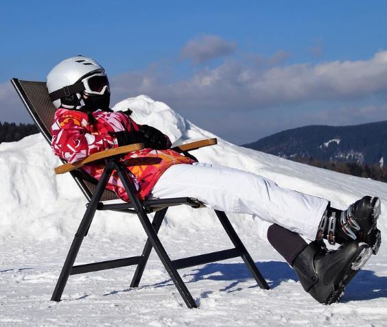 a skier lounging on a chair wearing skiing clothes and bootsa skier lounging on a chair wearing skiing clothes and boots