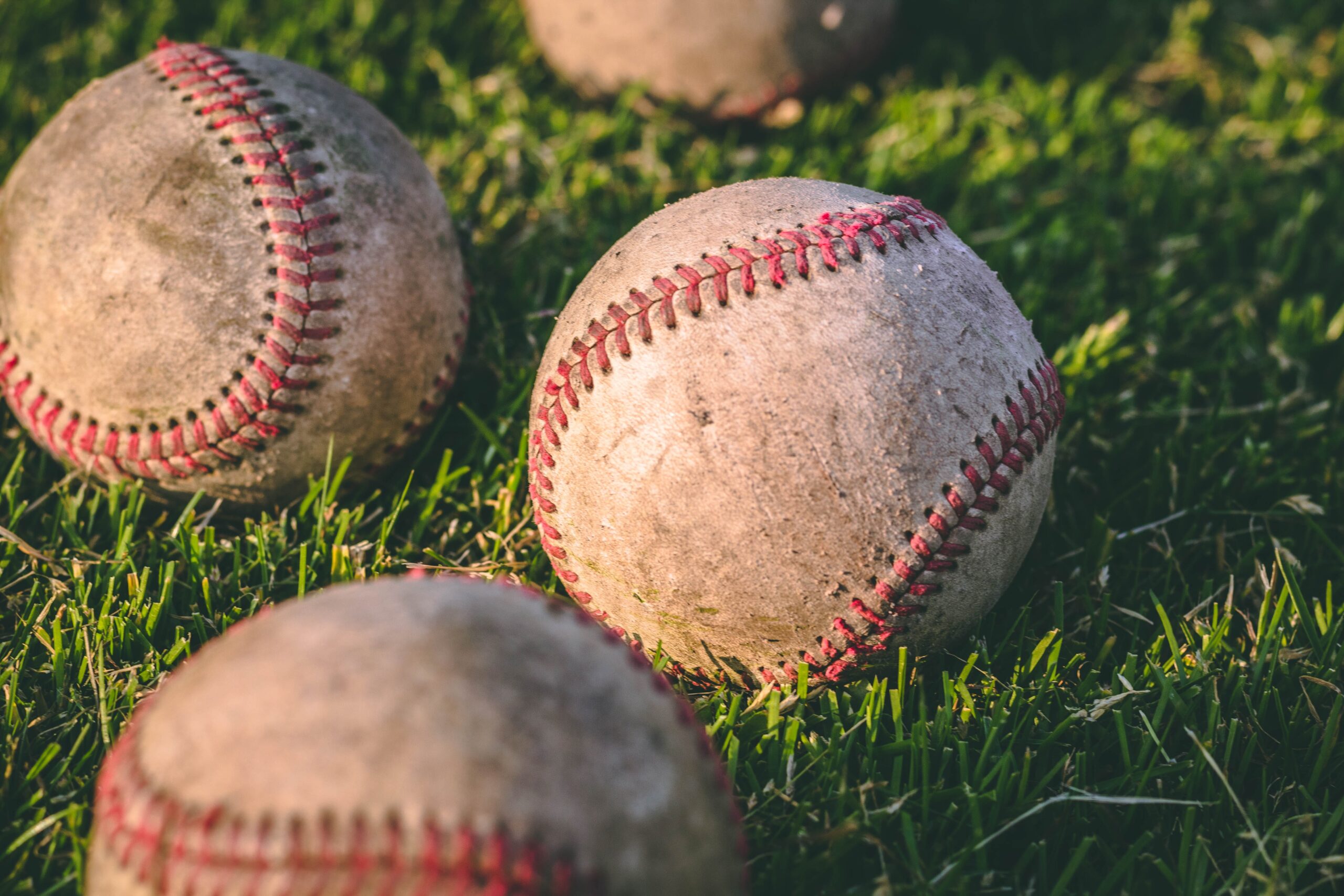 close-up-photography-of-four-baseballs-on-green-lawn-grasses